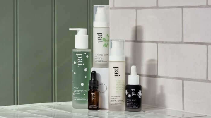Collection of Pai skincare products including cleanser, serum bottles and treatments arranged on marble surface against green paneled wall and white subway tiles