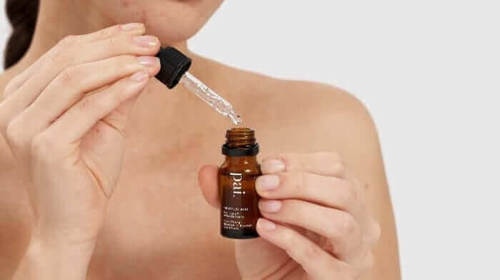 Woman applying amber glass dropper bottle skincare serum with pipette, demonstrating how to use facial oil booster
