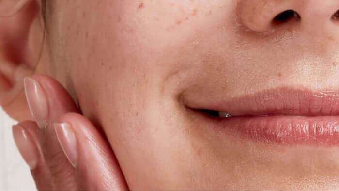 Close-up of woman's face showing smooth, hydrated skin with hand gently touching cheek, demonstrating healthy skincare results