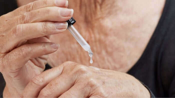 Hand dispensing clear serum drop from glass dropper bottle onto palm, showing skincare application technique