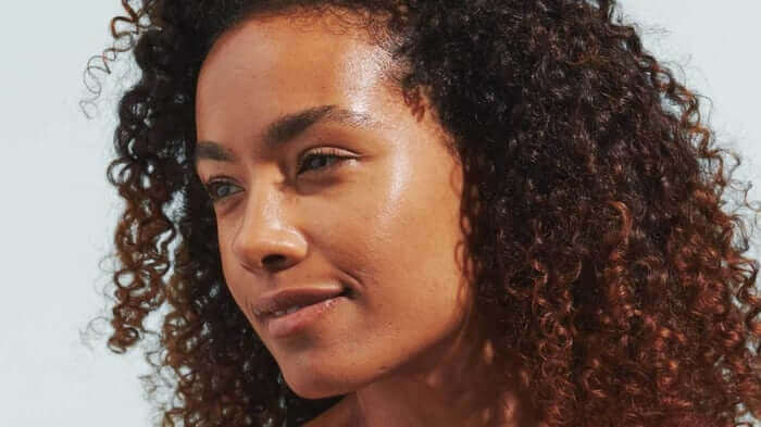 Woman with curly hair and dewy, healthy-looking skin showcasing natural radiance and moisture retention