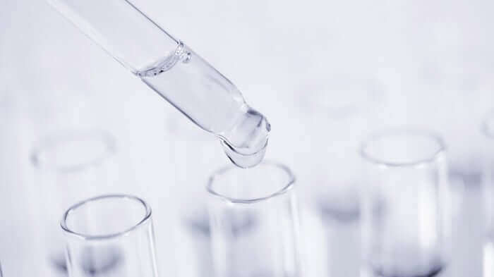 Clear glass dropper dispensing serum into test tubes in laboratory setting for skincare formulation research
