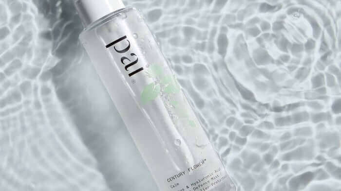 Pai Century Flower face mist bottle with clear liquid and green botanical elements, photographed against rippling water surface