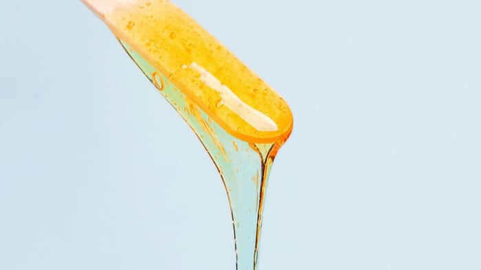 Golden honey dripping from wooden dipper, showing natural ingredients for sensitive skin waxing alternatives