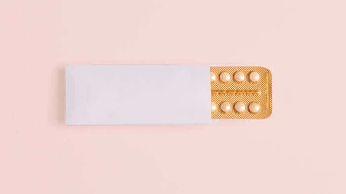 White pill packet with orange blister pack containing birth control pills on pink background