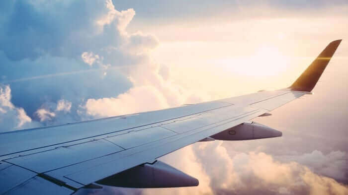 Airplane wing view from window seat showing clouds and sky during flight, illustrating travel skincare challenges
