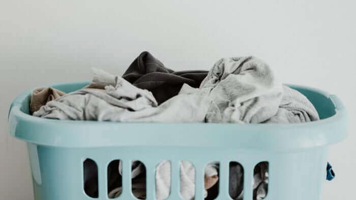 Turquoise laundry basket filled with mixed dark and light colored clothes against white background