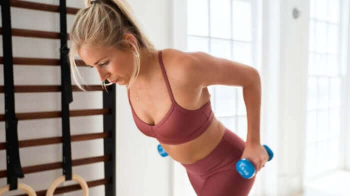Woman exercising with blue dumbbells in gym wearing burgundy workout clothes, relevant to exercise and acne skincare concerns