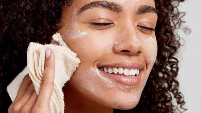 Woman with curly hair gently cleansing face with cream muslin cloth, showing gentle skincare routine
