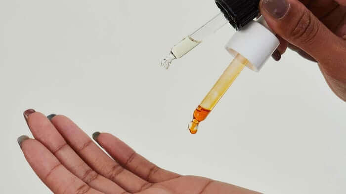 Hand receiving drops of golden facial oil from dropper bottle, demonstrating how to apply skincare booster serum