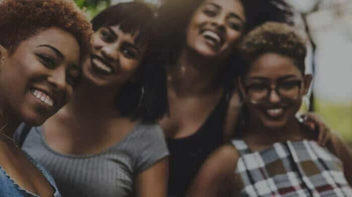 Four diverse women laughing and embracing together, showing genuine happiness and friendship connection