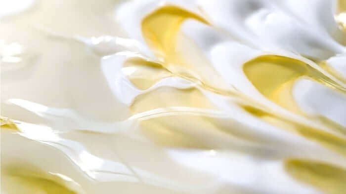 Close-up of creamy white moisturizer with golden oil droplets showing rich, hydrating texture for skincare