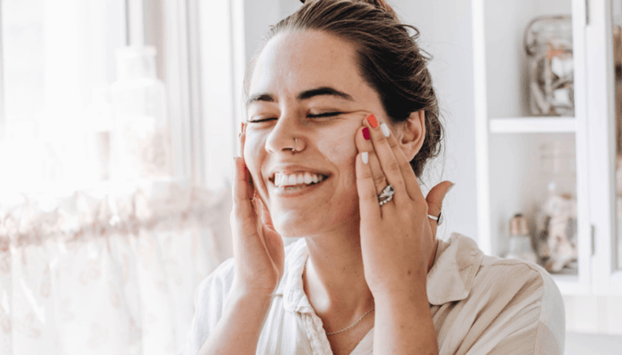 Woman with eyes closed gently applying skincare to her face with both hands, enjoying her daily routine