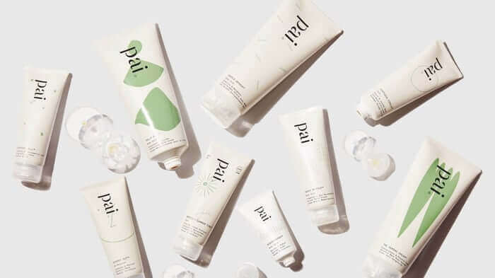Pai Skincare natural skincare products with white and green packaging scattered artistically on white background, featuring various face creams and serums for sustainable beauty routine