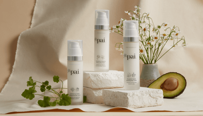 Three Pai Skincare moisturisers displayed on natural stone blocks with chamomile flowers, herbs and avocado half