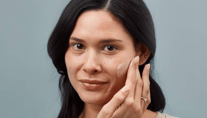Woman applying cream to her cheek during at-home facial routine for sensitive skin