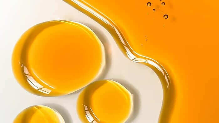 Golden rosehip oil droplets and flowing texture on cream background showing the rich, nourishing consistency