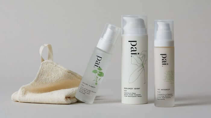 Pai Skincare cleanser and serum in white pump bottles with natural loofah sponge on neutral background