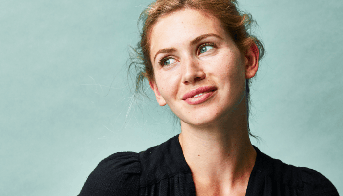 Woman with clear, healthy-looking skin smiling gently against soft green background