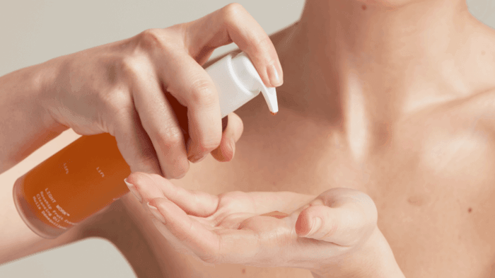 Hands dispensing orange facial cleanser from pump bottle into palm for double cleansing routine