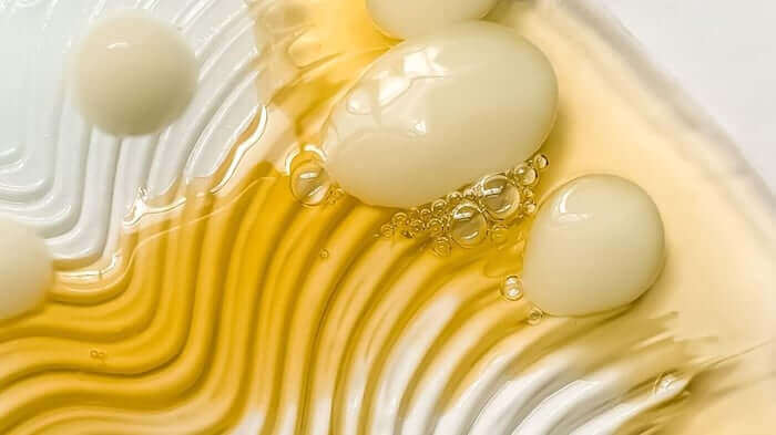 Golden facial oil with bubbles creating flowing ripple patterns, showing the lightweight texture ideal for combination skin care