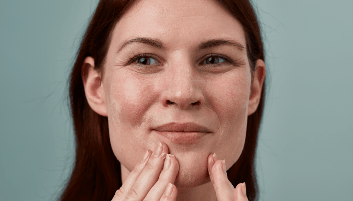 Woman with radiant skin gently touching her face after gentle exfoliation, demonstrating healthy sensitive skin care routine