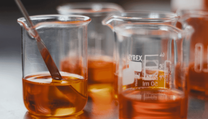 Laboratory beakers and measuring glasses containing golden-orange facial oils in various stages of oxidation