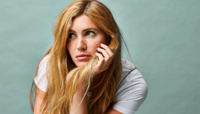 Young woman with long blonde hair touching her face, looking concerned about skin health against soft mint background