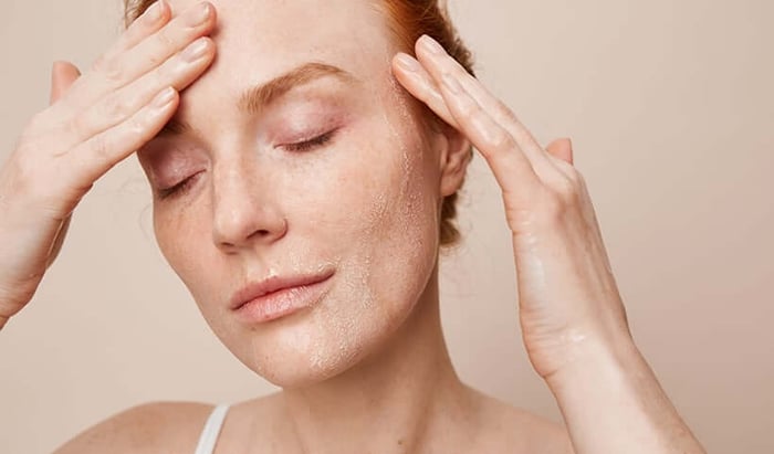 Woman with closed eyes gently applying skincare product around eye area with both hands for sensitive skin care