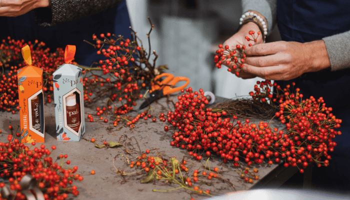 Hands arranging red rosehip berries and twigs around Pai Skincare product boxes for festive Christmas wreath making