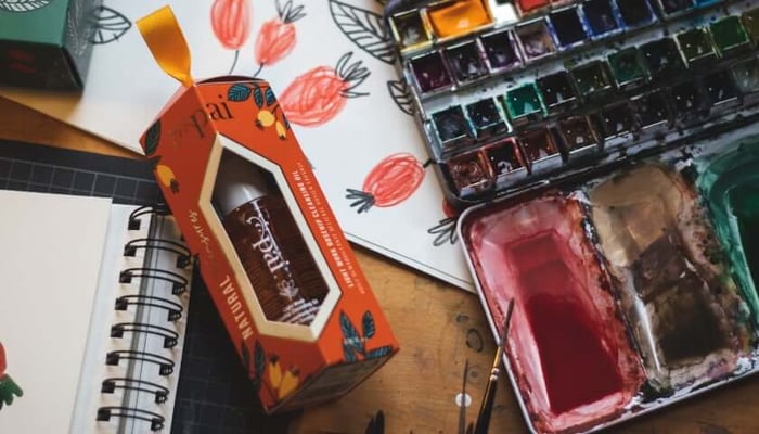 Artist workspace featuring Pai Skincare Natural Treasures Light Work gift box with botanical illustrations alongside watercolor paints and sketchbook