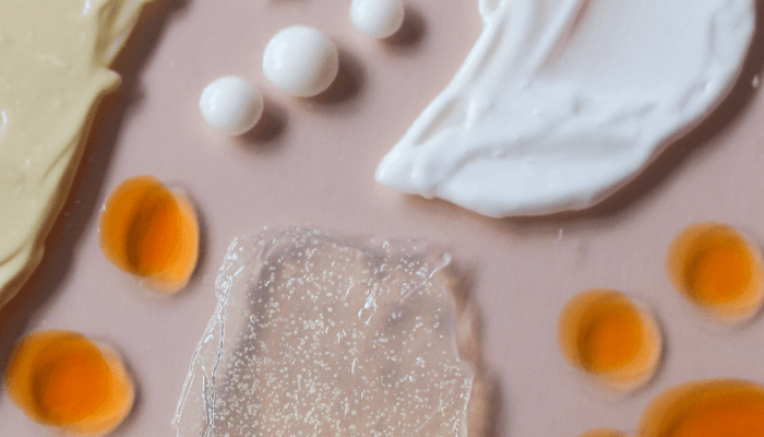 Clear gel texture and white cream swatches with orange rosehip oil drops on pink background