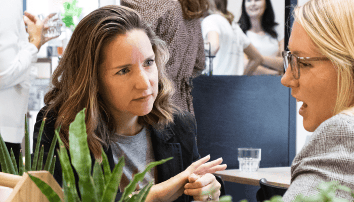 Two women having an intimate conversation at a cafe table, one appearing to share personal experiences with supportive listener