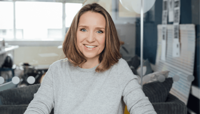 Sarah Brown, Pai Skincare founder, smiling warmly in grey sweater in modern office with skincare products