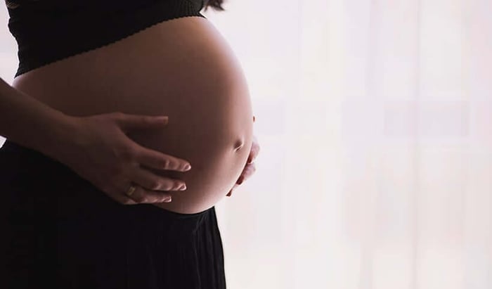 Pregnant woman gently cradling her bare belly, representing natural pregnancy skincare and stretch mark prevention
