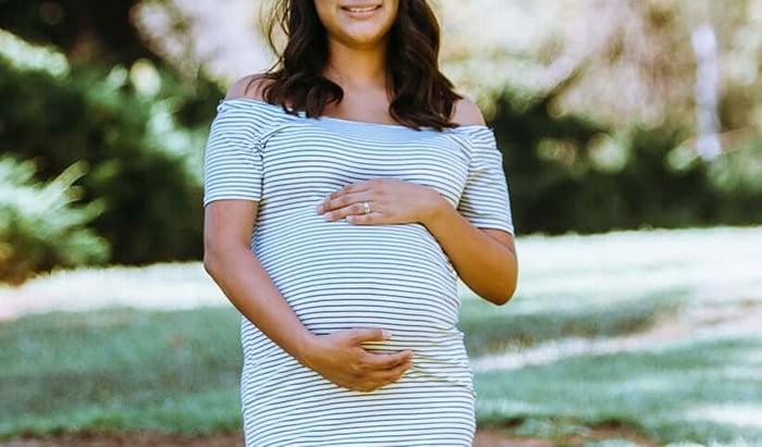 Pregnant woman in striped dress cradling her bump outdoors, representing safe pregnancy skincare choices
