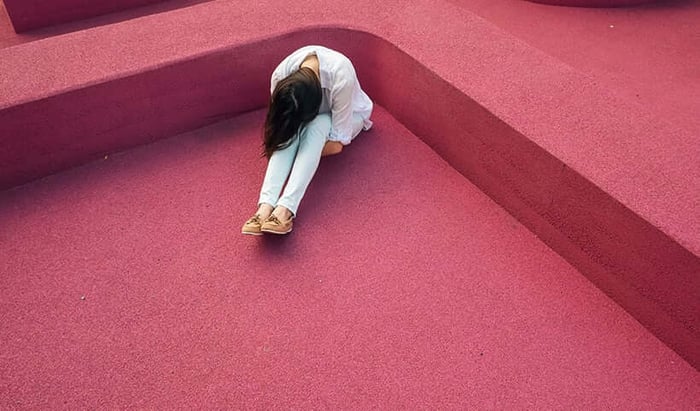 Woman sitting alone on pink concrete steps with her head down, expressing vulnerability and isolation