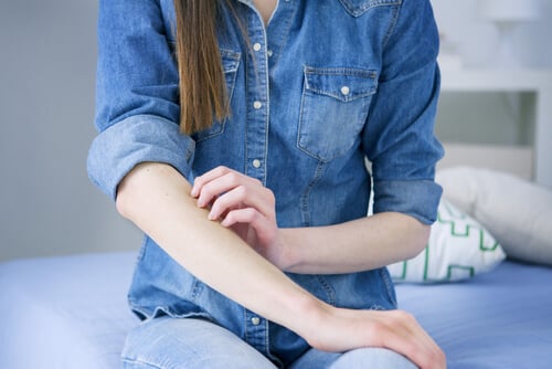 Woman in denim shirt scratching itchy skin on her forearm