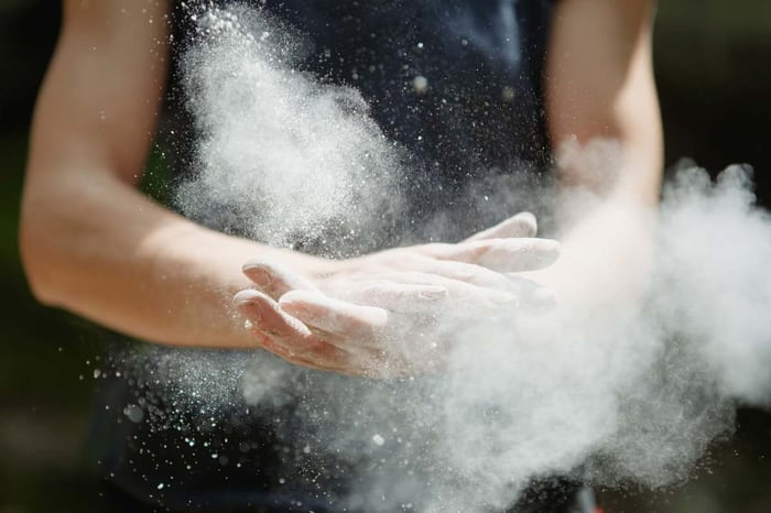 Hands cupping white clay powder dispersing into clouds against dark background