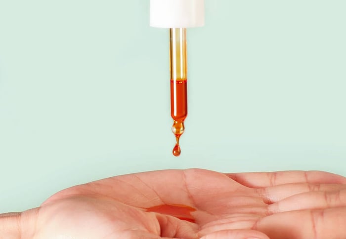 Golden rosehip oil drop falling from dropper into cupped hands against soft green background