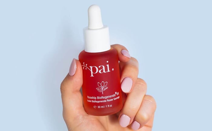 Hand holding Pai Rosehip BioRegenerate Oil bottle with red-orange natural oil and white dropper cap