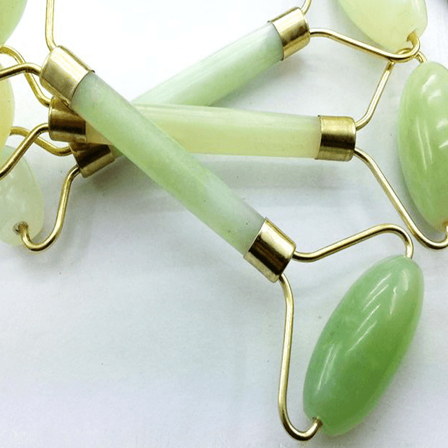 Jade roller facial massage tools with green stone heads and gold metal frames on white surface