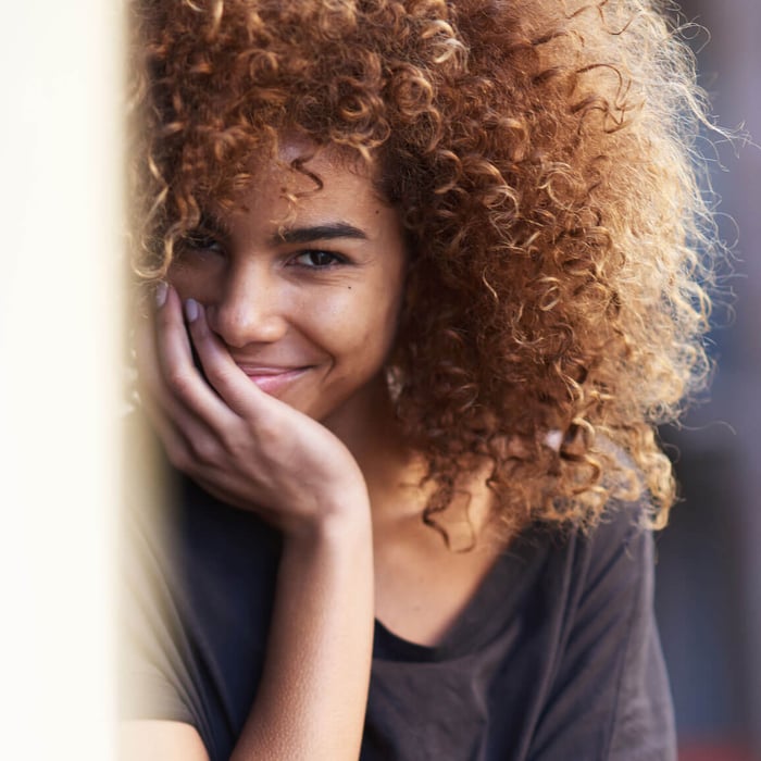 Smiling woman with curly hair gently touching her clear, healthy chin and jawline with her hand