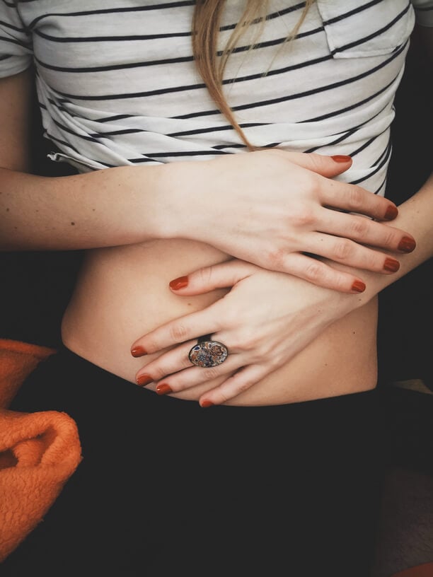 Woman in striped top cradling stomach with both hands, suggesting digestive wellness and gut health awareness