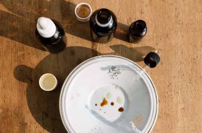 White ceramic plate with essential oil drops and natural ingredients surrounded by dark glass bottles on wooden surface