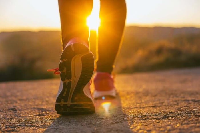 Running shoes on sunlit road at sunrise during morning exercise routine