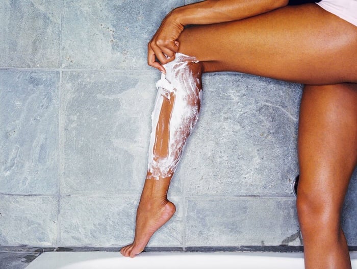 Woman applying gentle shaving cream to her leg on bathroom tiles to prevent irritation and red bumps