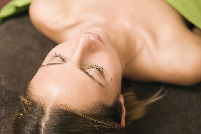 Woman with glowing skin lying relaxed after skincare treatment, eyes closed peacefully