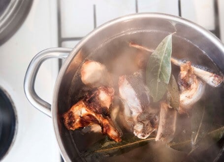 Simmering bone broth with bay leaves in stainless steel pot, rich in collagen for skin health
