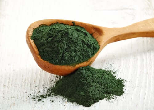 Green spirulina powder spilling from wooden spoon onto white surface